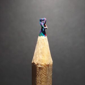 Close-up of two intricately carved hearts entangled together at the tip of a sharpened pencil, showcasing detailed miniature craftsmanship and delicate design on graphite.