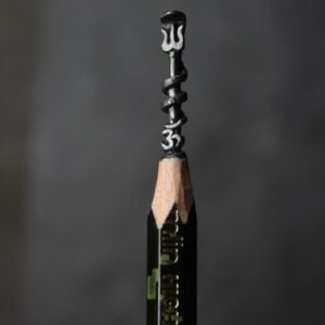 Close-up of a hand-carved Trishul placed above an Om symbol on the graphite tip of a pencil, symbolizing Lord Shiva and spiritual craftsmanship in miniature form